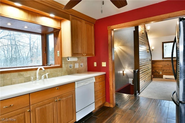 kitchen featuring white dishwasher, ceiling fan, sink, a baseboard radiator, and wood walls