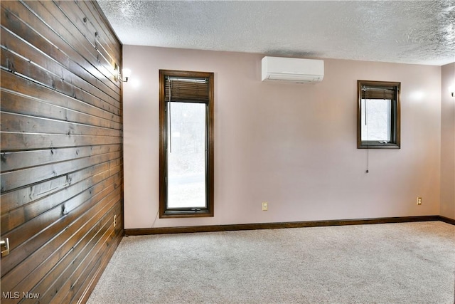 carpeted spare room featuring an AC wall unit, a textured ceiling, and wooden walls