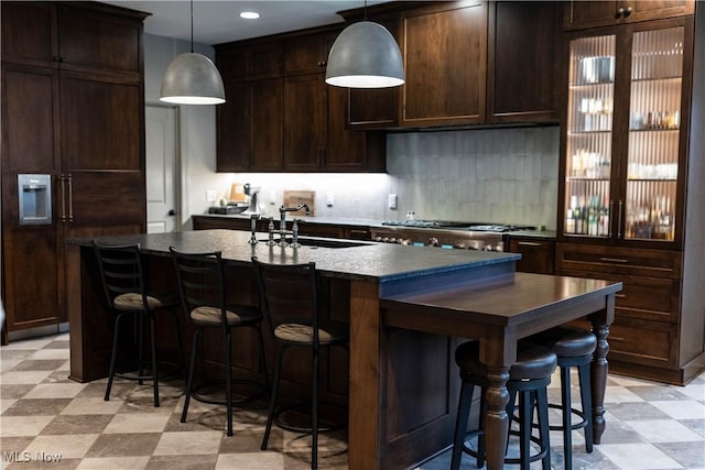 kitchen with sink, hanging light fixtures, a kitchen breakfast bar, dark brown cabinetry, and an island with sink