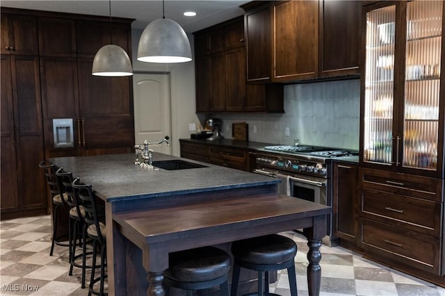 kitchen featuring pendant lighting, sink, a kitchen island with sink, dark brown cabinets, and a kitchen bar