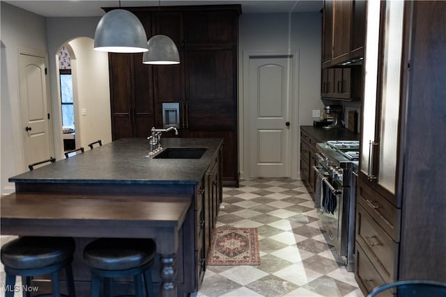 kitchen with sink, a kitchen island with sink, stainless steel range, a kitchen bar, and decorative light fixtures