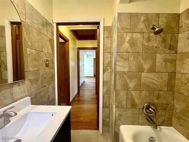 bathroom with tiled shower / bath, vanity, and tile walls