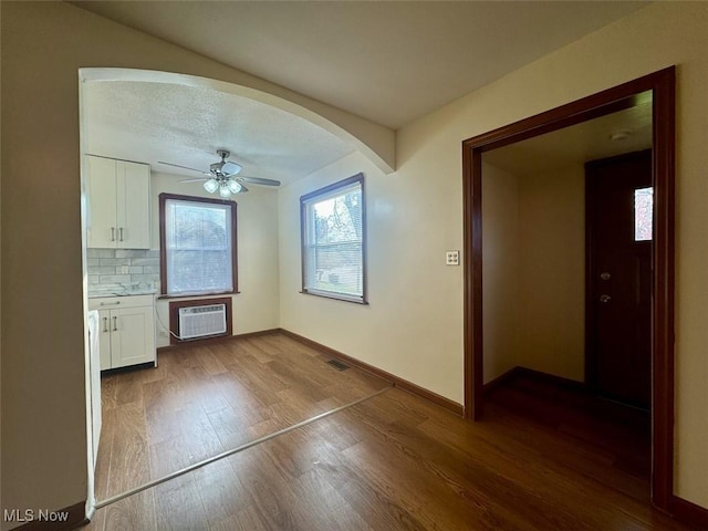 unfurnished dining area with wood-type flooring, a wall unit AC, and ceiling fan