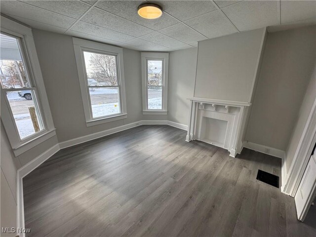 unfurnished living room featuring a drop ceiling and dark wood-type flooring