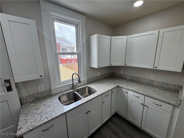 kitchen with light stone counters, sink, white cabinets, and dark hardwood / wood-style floors