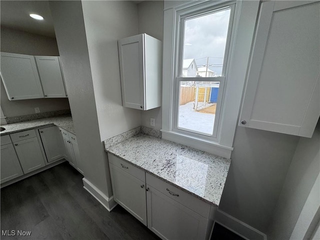 kitchen with white cabinetry, a wealth of natural light, dark wood-type flooring, and light stone counters