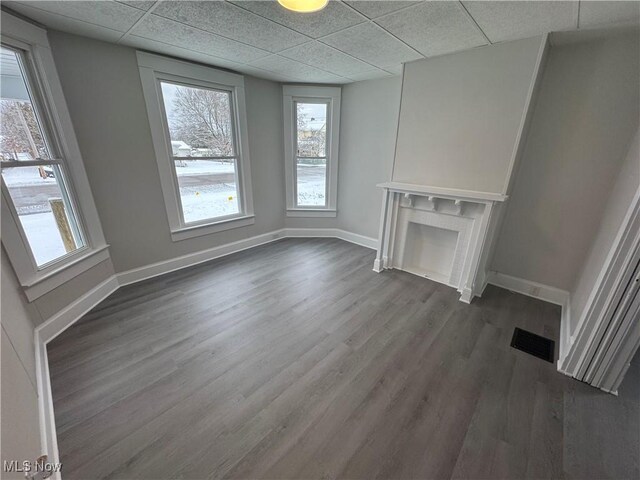 unfurnished living room featuring a paneled ceiling, dark hardwood / wood-style floors, and plenty of natural light