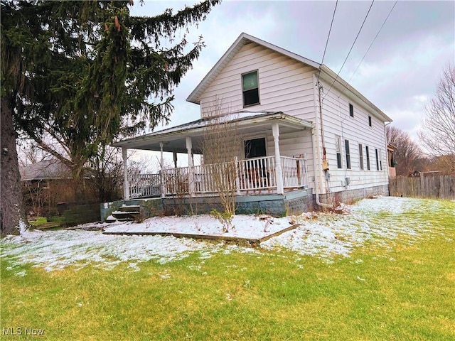 snow covered back of property with a lawn and covered porch