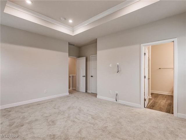 unfurnished bedroom with carpet floors, a raised ceiling, and connected bathroom