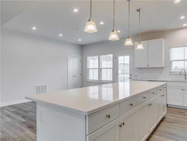 kitchen with a center island, white cabinetry, hanging light fixtures, and sink