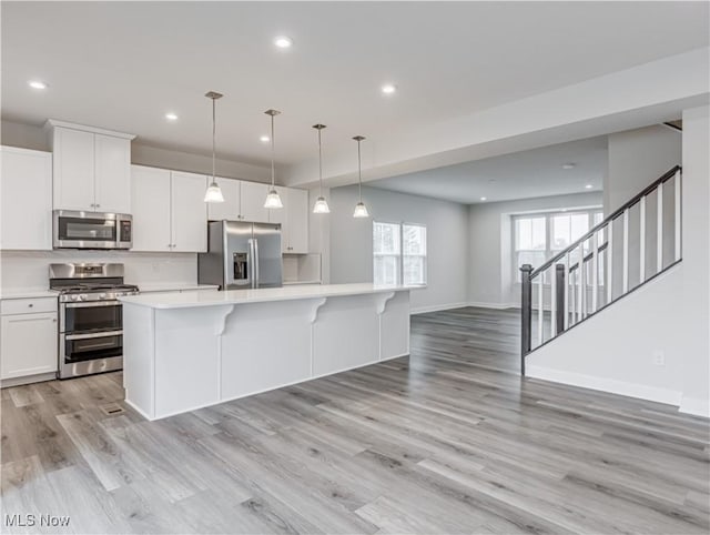 kitchen featuring appliances with stainless steel finishes, white cabinets, light hardwood / wood-style floors, a kitchen island, and hanging light fixtures