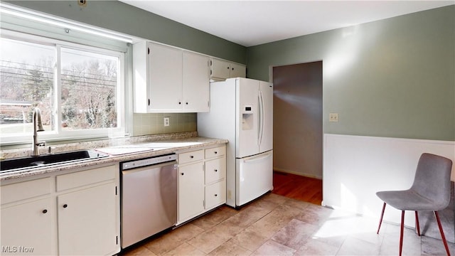 kitchen with tasteful backsplash, stainless steel dishwasher, sink, white refrigerator with ice dispenser, and white cabinetry