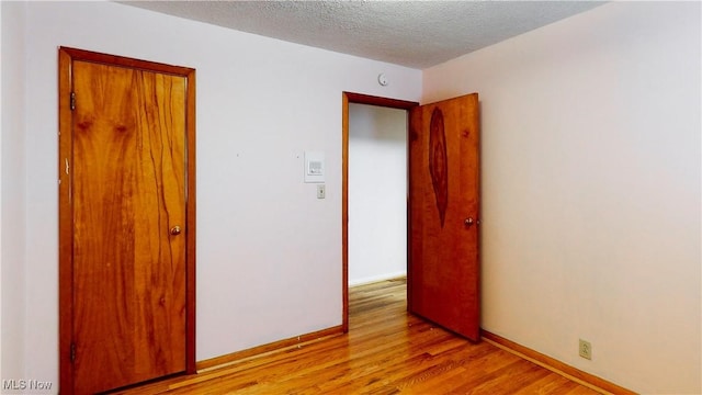 empty room with light wood-type flooring and a textured ceiling