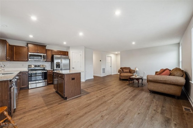 kitchen with light stone countertops, sink, appliances with stainless steel finishes, a kitchen island, and hardwood / wood-style flooring