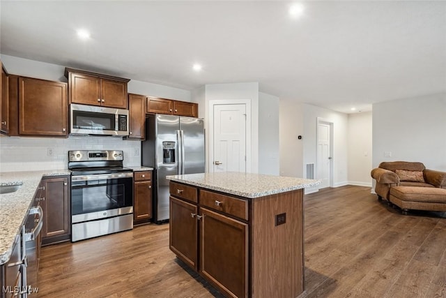 kitchen with a center island, backsplash, dark wood-type flooring, light stone countertops, and appliances with stainless steel finishes