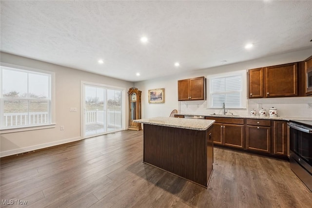 kitchen with light stone countertops, stainless steel appliances, sink, a center island, and dark hardwood / wood-style floors