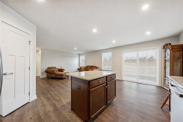 kitchen with dishwasher, a center island, light stone countertops, and dark wood-type flooring