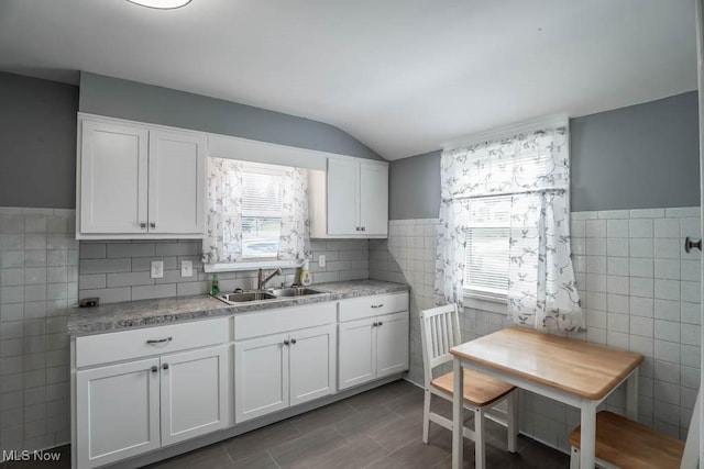 kitchen featuring tile walls, white cabinetry, sink, and vaulted ceiling