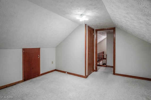 bonus room with vaulted ceiling, light carpet, and a textured ceiling