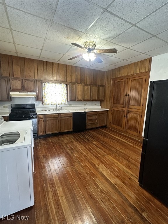 kitchen featuring ceiling fan, sink, dark hardwood / wood-style floors, wooden walls, and black appliances