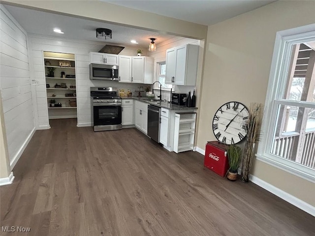 kitchen featuring white cabinetry, sink, dark hardwood / wood-style flooring, wooden walls, and appliances with stainless steel finishes