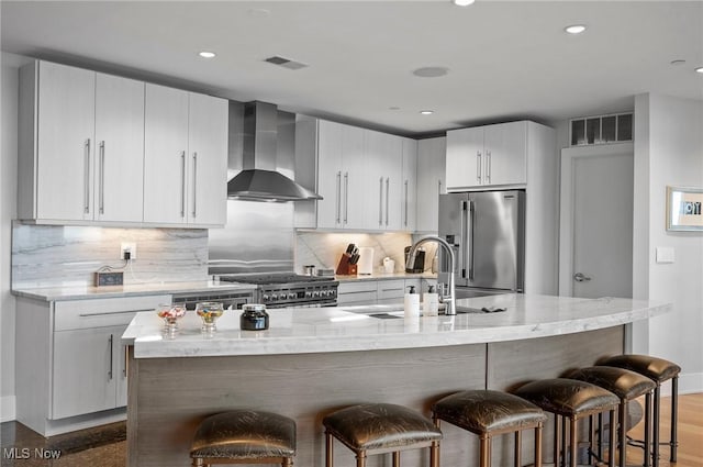 kitchen with a kitchen island with sink, sink, wall chimney exhaust hood, and high end appliances