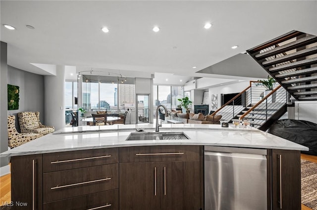 kitchen with light stone countertops, dishwasher, sink, light hardwood / wood-style flooring, and an island with sink