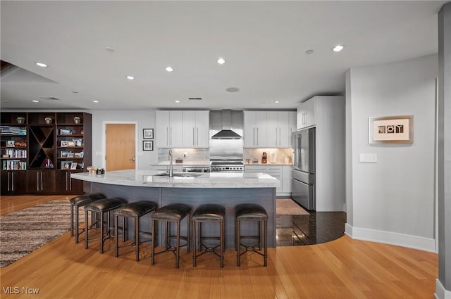 kitchen featuring appliances with stainless steel finishes, a kitchen island with sink, sink, wall chimney range hood, and white cabinetry