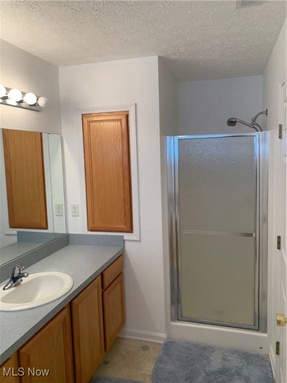 bathroom featuring vanity, a shower with shower door, and a textured ceiling