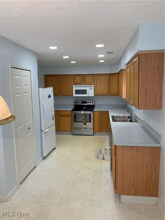 kitchen with a textured ceiling, white appliances, and sink