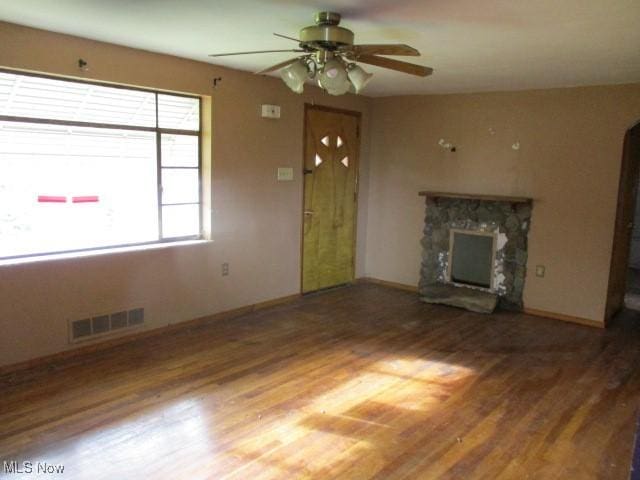 unfurnished living room featuring wood-type flooring, a stone fireplace, and ceiling fan