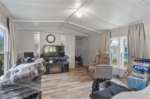 living room featuring vaulted ceiling with beams, a fireplace, and light hardwood / wood-style floors