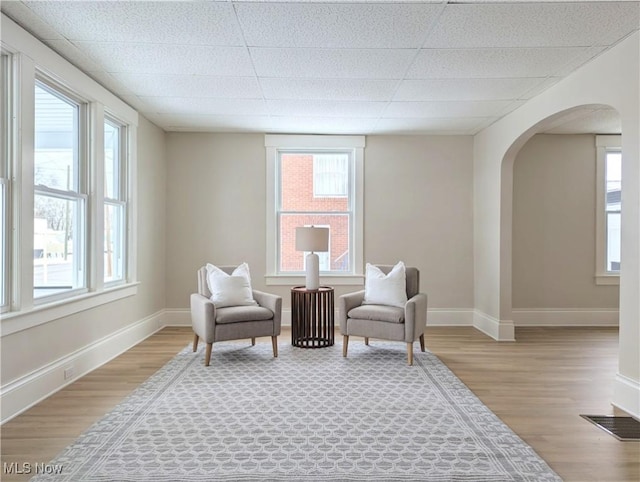 sitting room featuring light hardwood / wood-style floors, a drop ceiling, and a healthy amount of sunlight