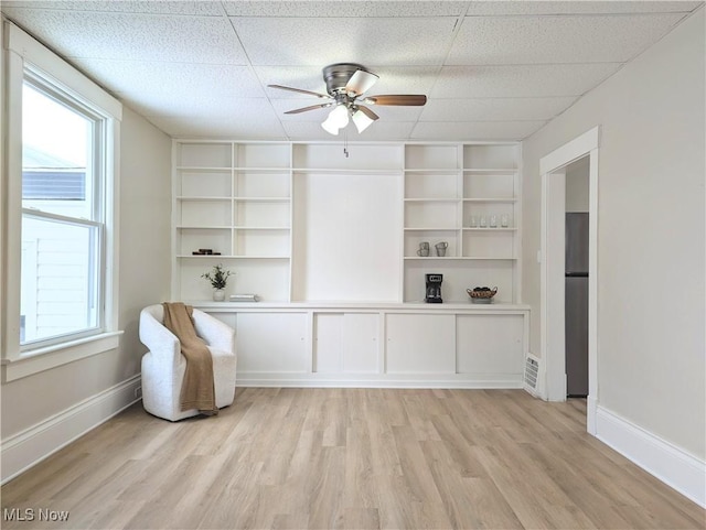 interior space featuring a paneled ceiling, built in shelves, ceiling fan, and light wood-type flooring