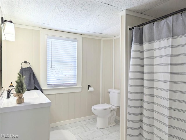 bathroom featuring a paneled ceiling, wooden walls, vanity, and toilet