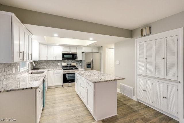 kitchen with white cabinetry, sink, stainless steel appliances, decorative backsplash, and a kitchen island