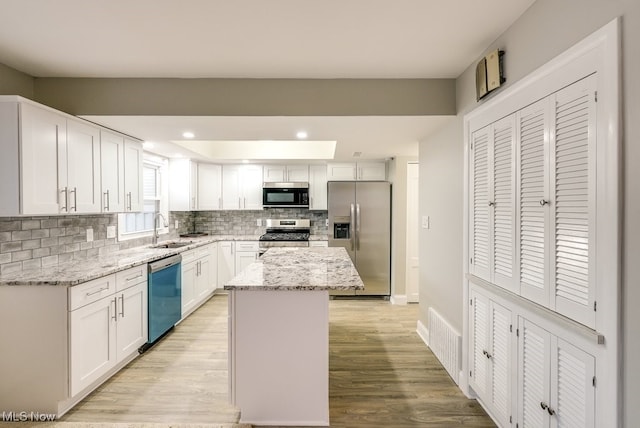 kitchen featuring white cabinetry, a center island, stainless steel appliances, and light stone counters