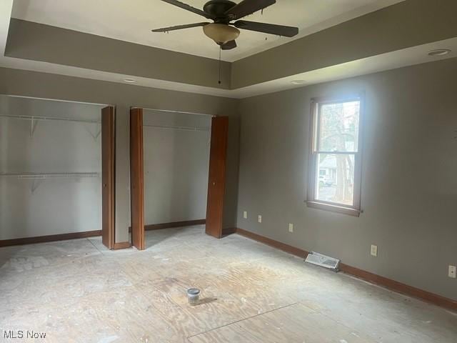 unfurnished bedroom featuring a tray ceiling, multiple closets, and ceiling fan