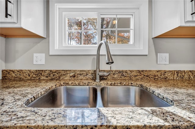 room details featuring white cabinets, light stone countertops, and sink