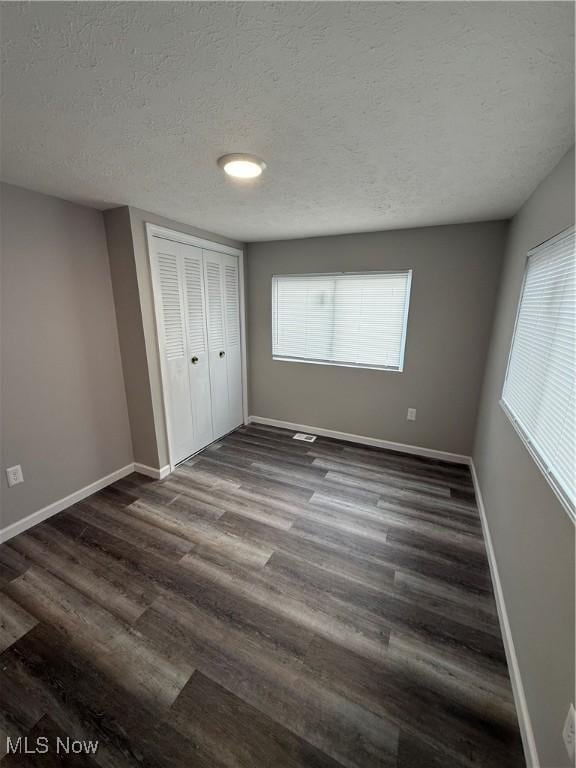 unfurnished bedroom with dark hardwood / wood-style flooring, a textured ceiling, and a closet