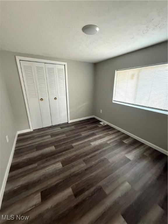 unfurnished bedroom with dark wood-type flooring and a closet