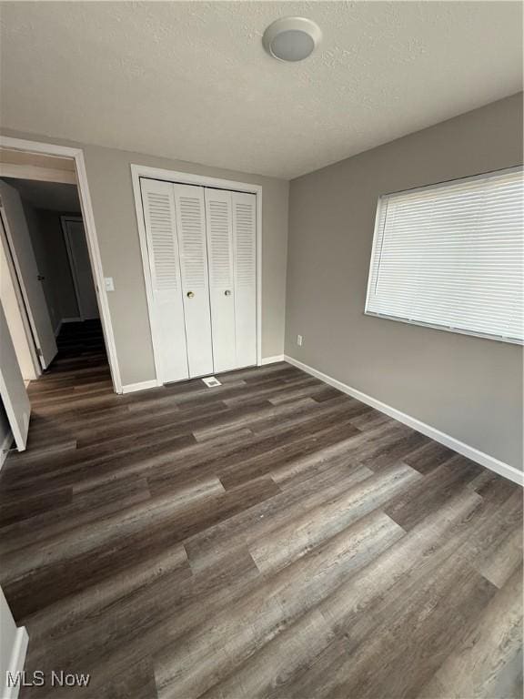 unfurnished bedroom with a textured ceiling, dark hardwood / wood-style flooring, and a closet