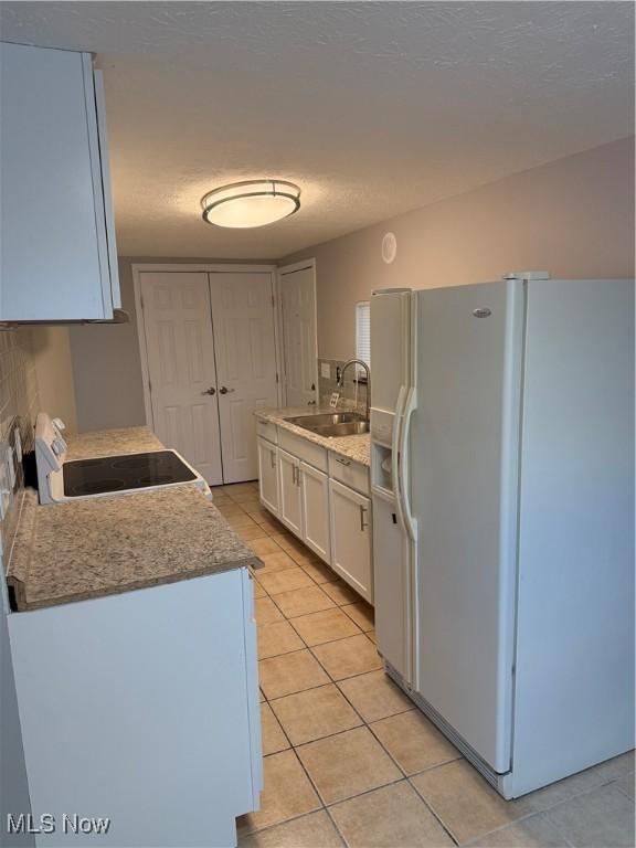 kitchen with white fridge with ice dispenser, sink, white cabinets, stove, and light tile patterned floors