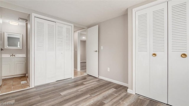 unfurnished bedroom with baseboards, ensuite bath, a sink, light wood-style floors, and a closet