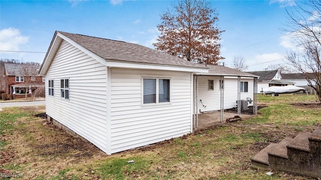 view of side of property with central AC unit, a lawn, and roof with shingles