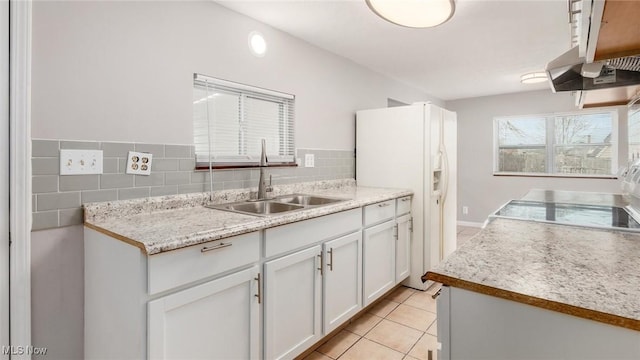 kitchen with light tile patterned flooring, a sink, white cabinets, light countertops, and white fridge with ice dispenser