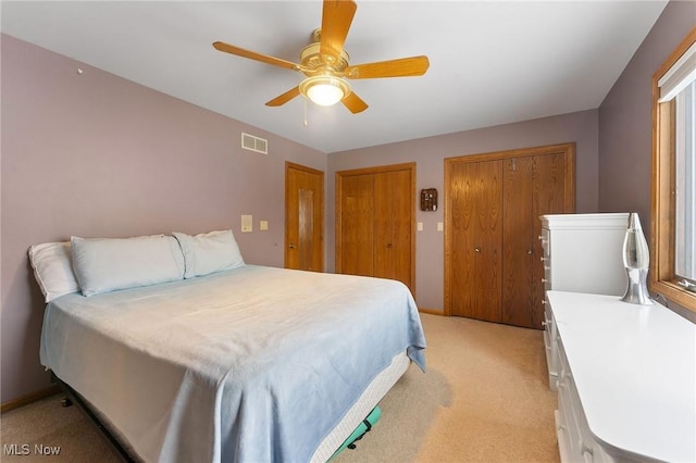 carpeted bedroom with ceiling fan and multiple closets