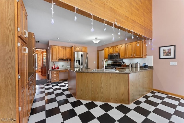 kitchen with kitchen peninsula, appliances with stainless steel finishes, dark stone counters, wooden walls, and sink