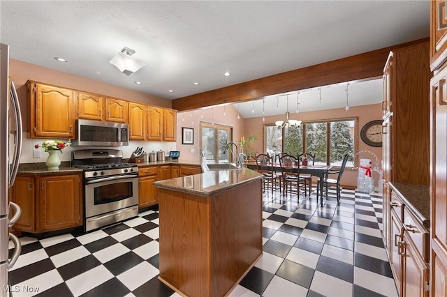 kitchen featuring rail lighting, stainless steel appliances, a kitchen island with sink, sink, and an inviting chandelier