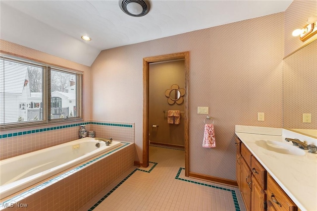 bathroom featuring tile patterned flooring, a relaxing tiled tub, vanity, and vaulted ceiling